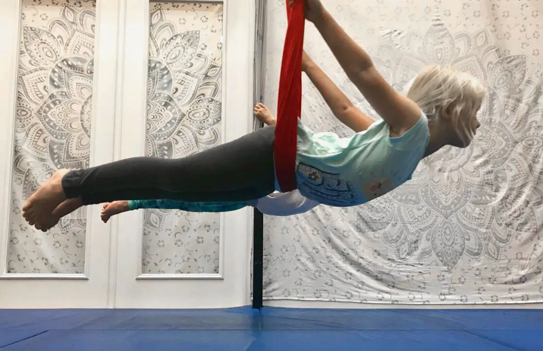 A student flies face-down in a red aerial silk at Yayso Yoga