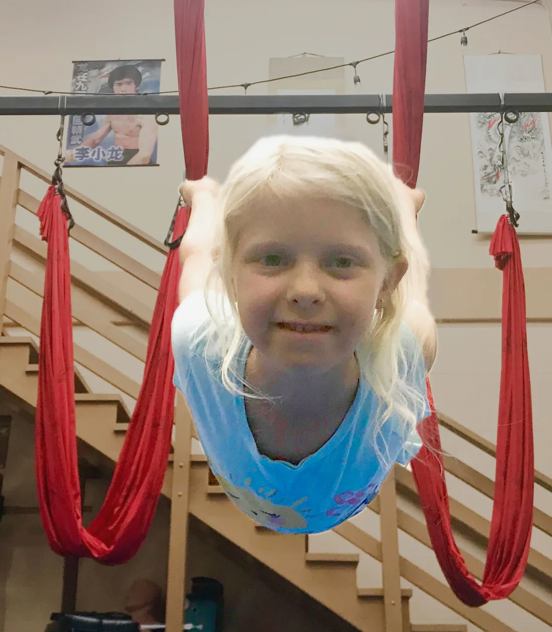 A smiling child hanging upside down in an aerial hammock